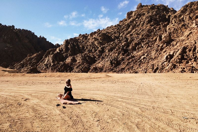 Woman sitting at desert against sky