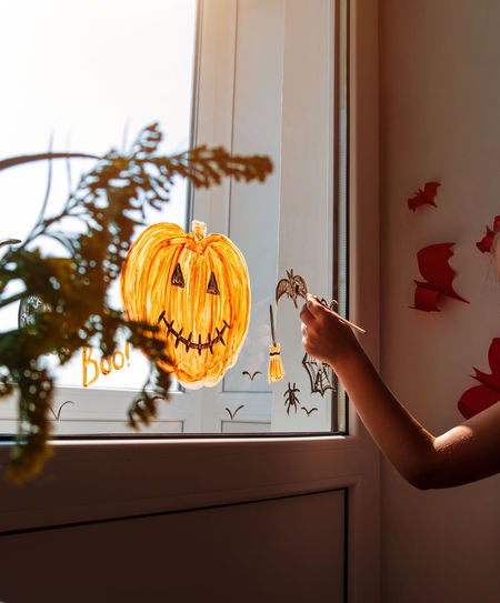 Child painting pumpkin on window preparing to celebrate halloween girl decorates room autumn holiday