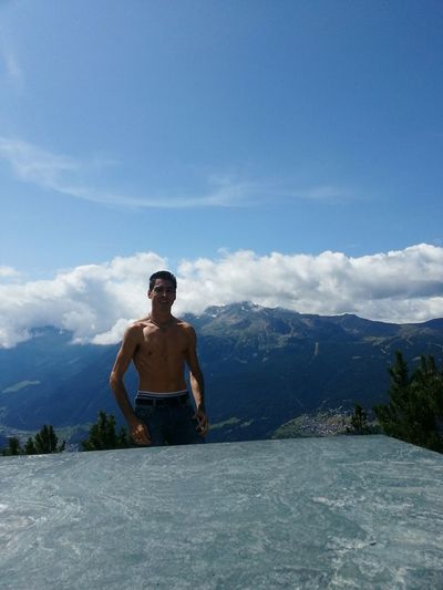 Shirtless man standing at granite by mountains against sky