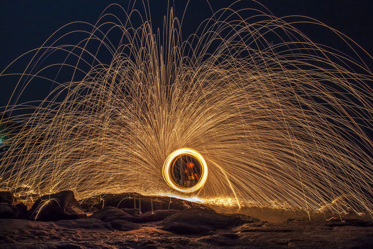 Person spinning wire wool at beach against sky