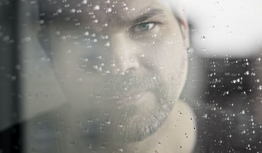 Close-up portrait of man seen through wet glass window