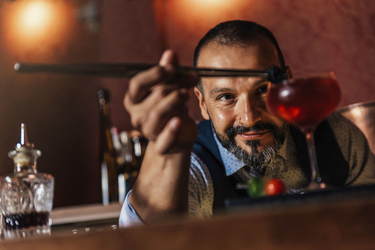 Portrait of smiling mature bartender preparing cocktail on bar counter