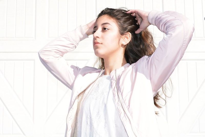Close-up of woman with hands in hair standing by white wall on sunny day