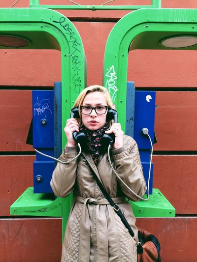 Portrait of young woman talking on telephone against wall