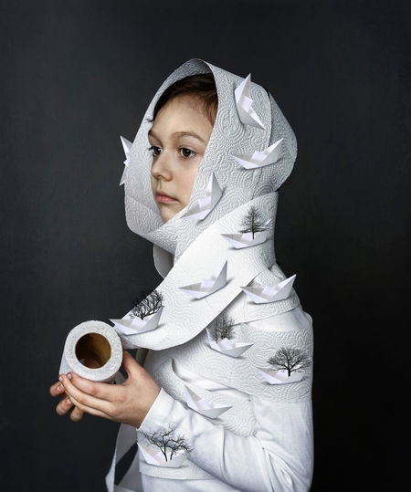 Portrait of a kid wrapped in toilet paper with paper ships against black background