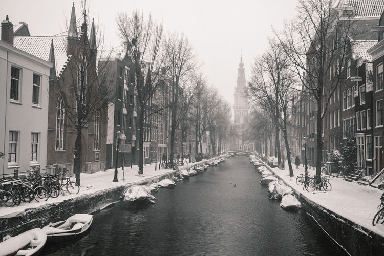 Canal amidst bare trees in city during winter