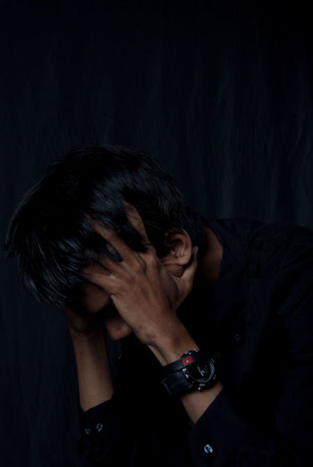 Sad young man with head in hands against black background