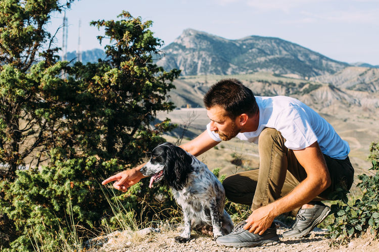 Male owner of spaniel dog walking against mountains background.