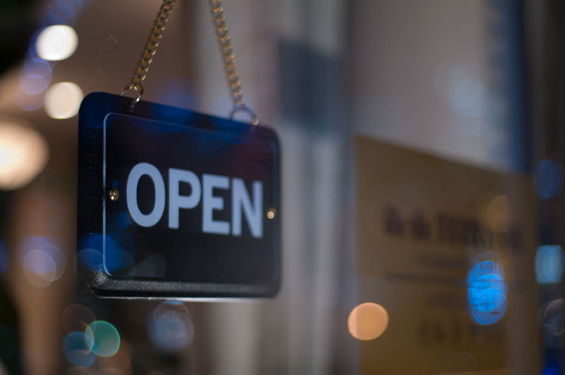 Close-up of open sign hanging from glass window of store