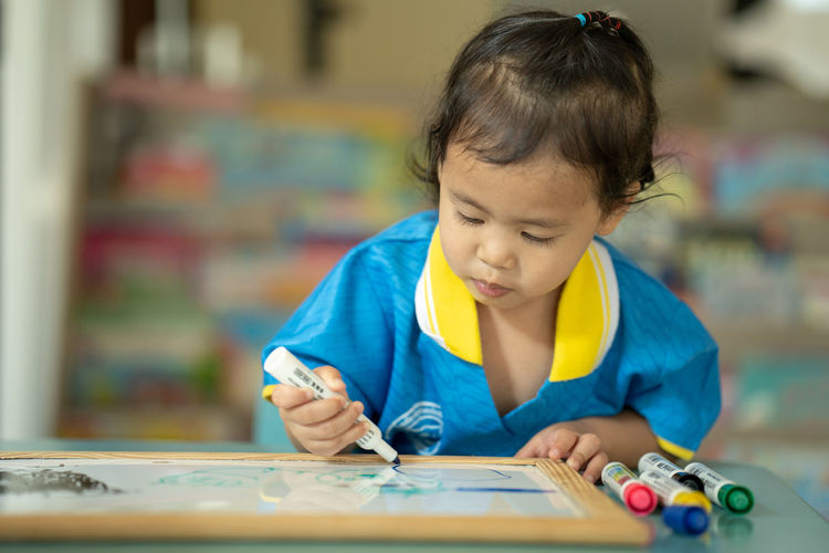 Cute little girl drawing on white board at table.