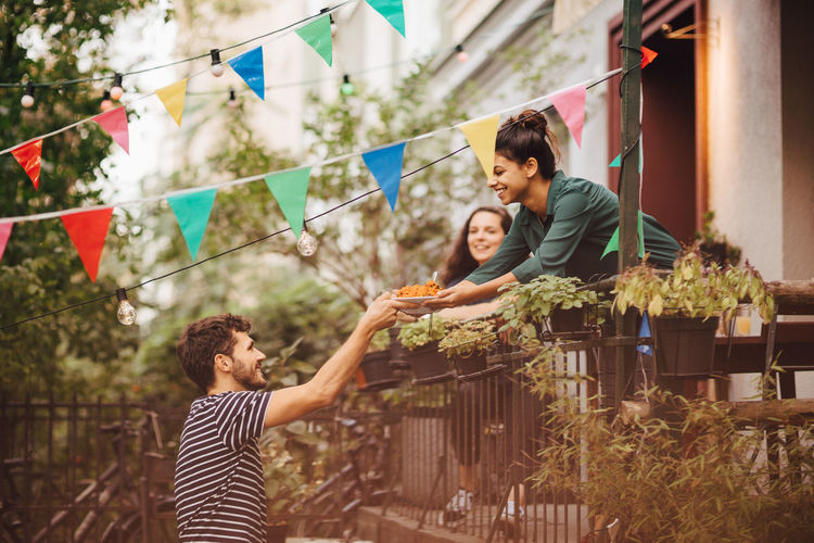 Smiling young woman giving food to male friend from balcony during garden party