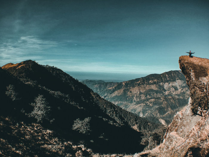 Mid distance view of young man sitting on mountain against sky