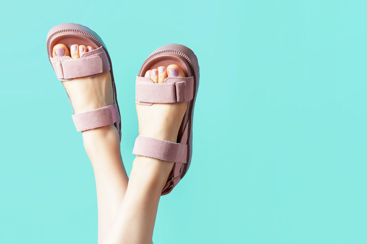 Female legs in pink sandals upside down on a blue background.