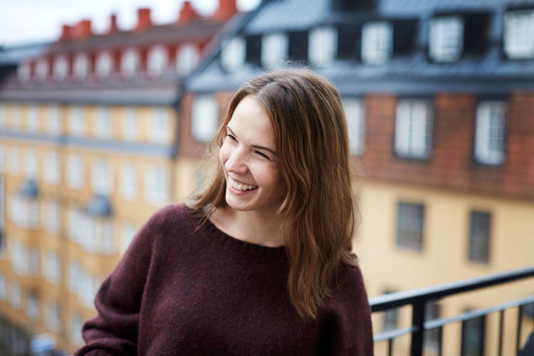 Smiling young woman standing in balcony at rental apartment