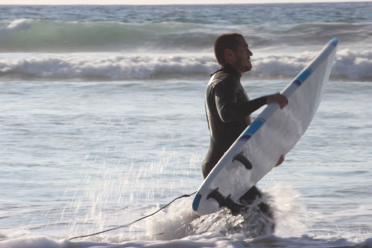 Man carrying surfboard in sea