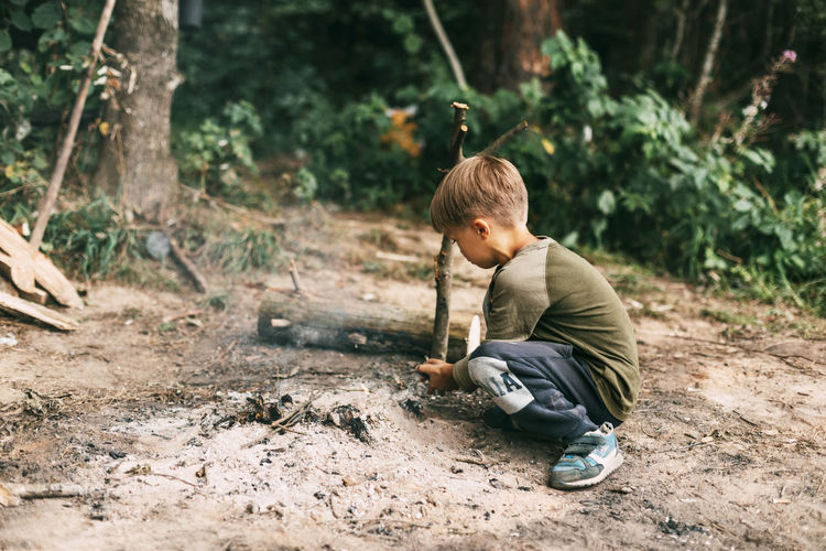 A boy-child makes a fire from wood branches in a forest camping. camping in the forest in summer. 