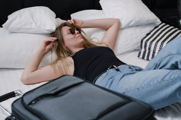 Woman with suitcase on bed in hotel having rest while traveling. traveler with bags top view.