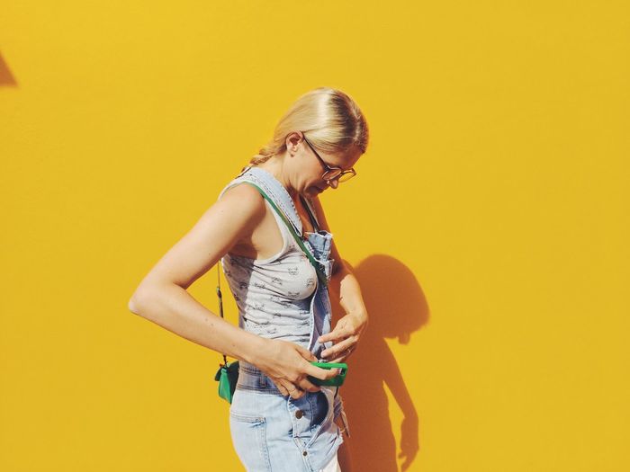 Side view of mid adult woman standing against yellow wall