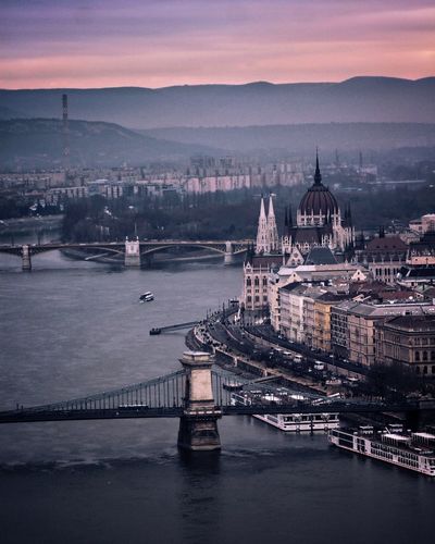 Bridge over river in city against sky during sunset