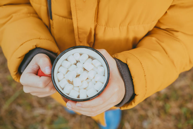 Hands of boy in a jacket hold hot cocoa with marshmallows in mugs, top view. a cozy photo with a mug 