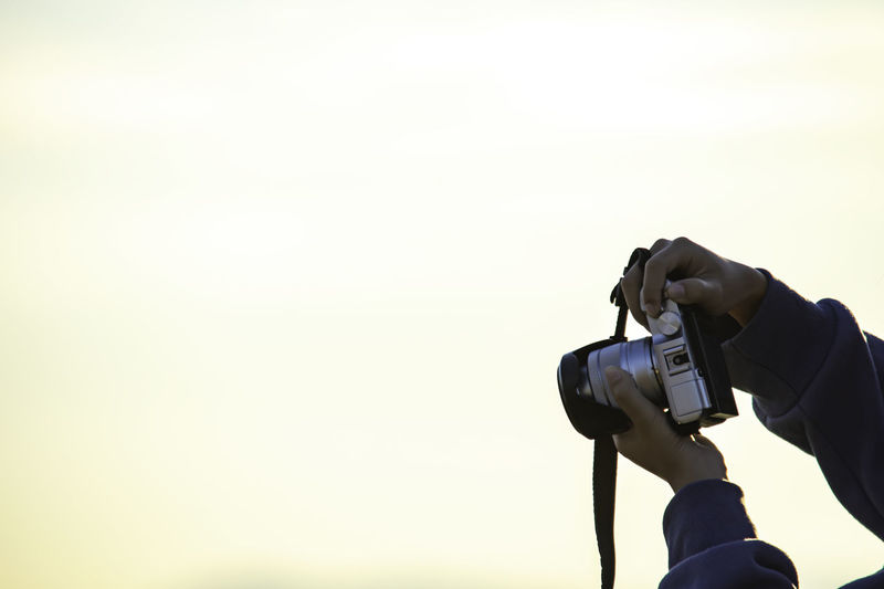 Man photographing camera against sky during sunset