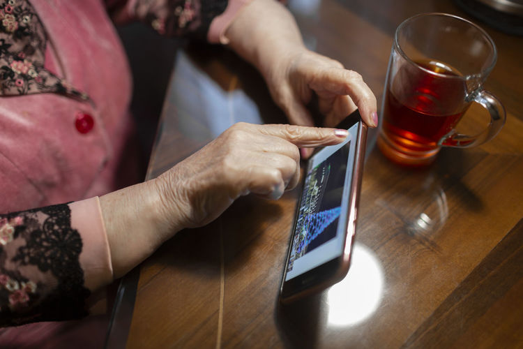 Senior woman touching screen of mobile phone on table at home
