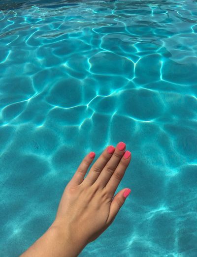 Cropped hand of woman showing nail polish over swimming pool