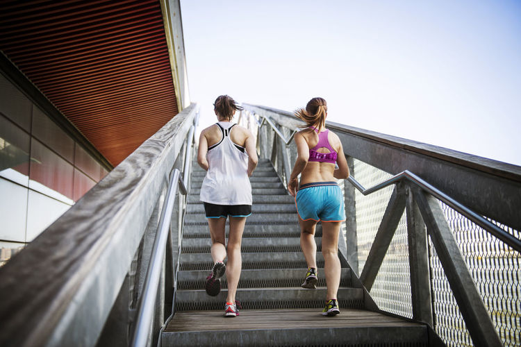 Rear view of women jogging on steps and staircases against clear sky