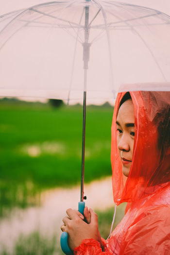 Side view of young woman carrying umbrella while standing on field during monsoon