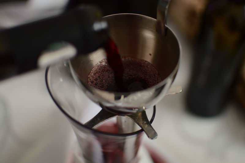 Cropped bottle pouring wine in glass from strainer