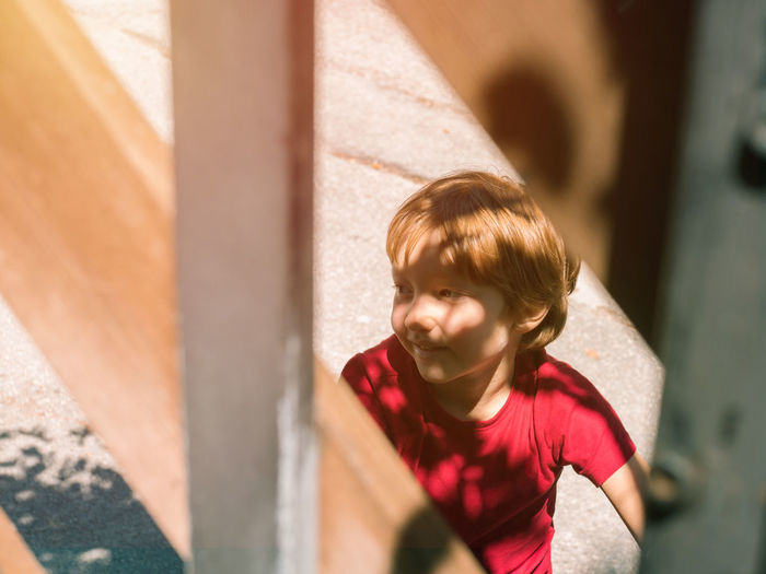 Little blonde boy wearing red t-shirt riding a bike outdoors in summer on a sunny day.