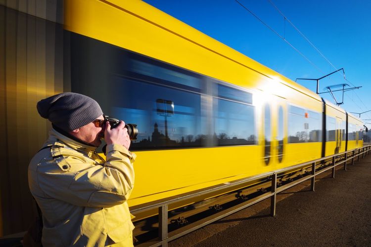 Side view of man photographing against moving train