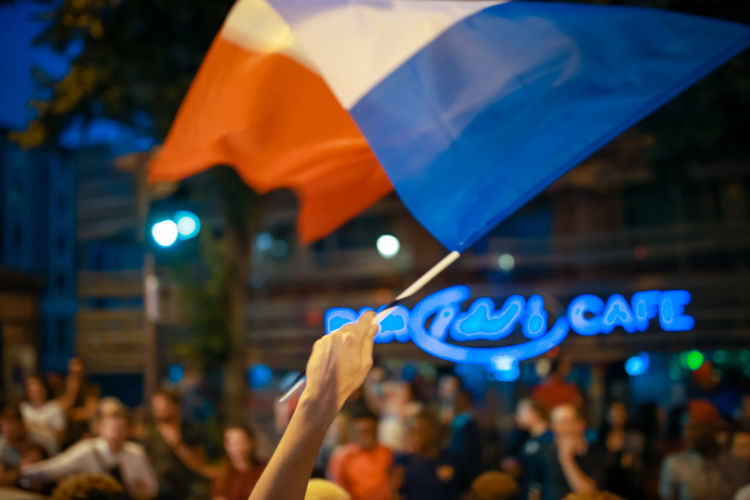Cropped hand waving french flag in city at dusk