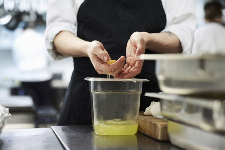Midsection of chef separating egg yolk from whites in commercial kitchen
