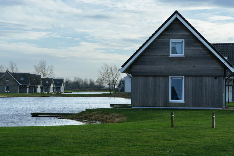 House by lake against sky