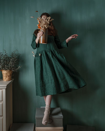 A young woman in a green linen dress making her creative self-portrait against a green wall