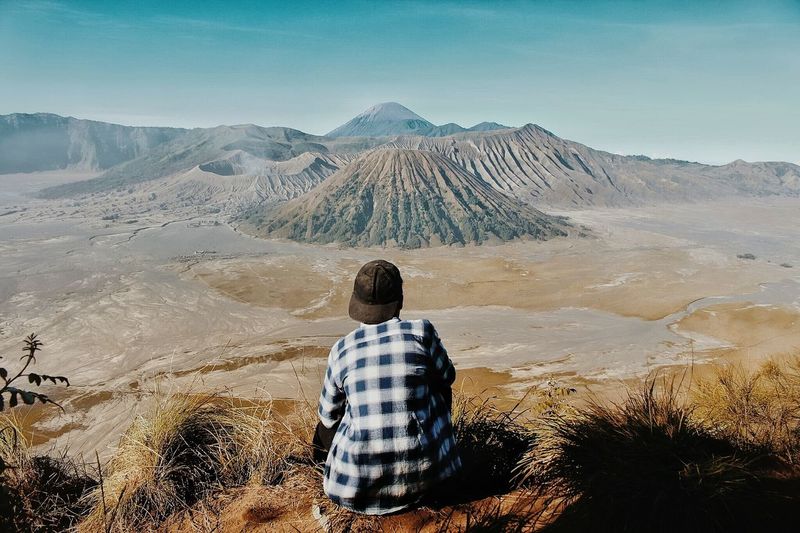 Rear view of man sitting on volcanic landscape