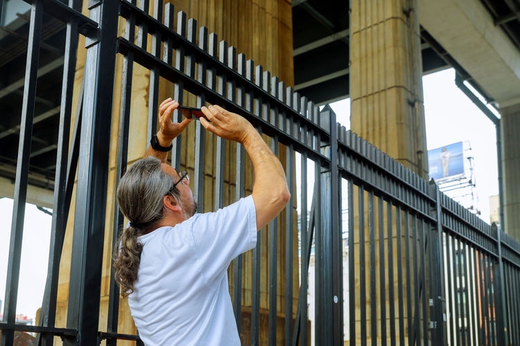 Mature man photographing while standing by fence
