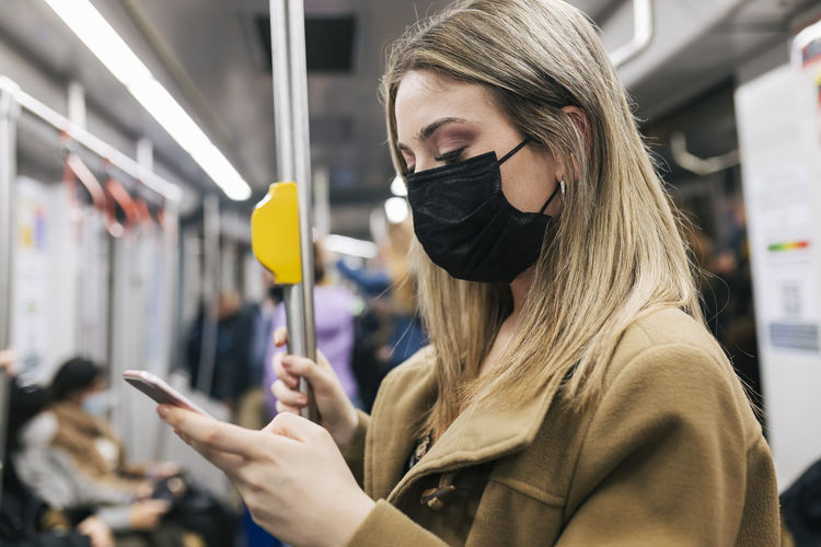 Passenger with protective face mask using smart phone in train