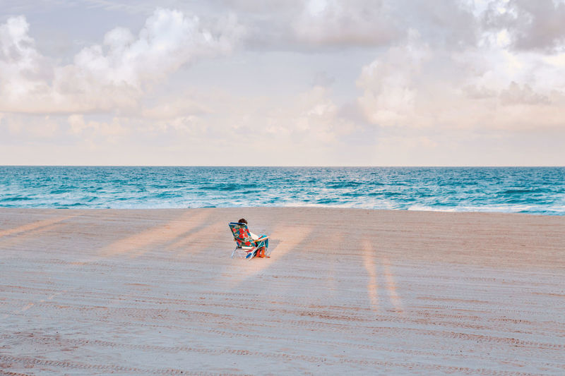 Man or woman sitting in beach chair on empty hollywood ocean beach in florida.  