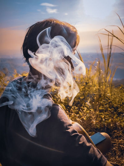 Close-up of man smoking on street against sky during sunset
