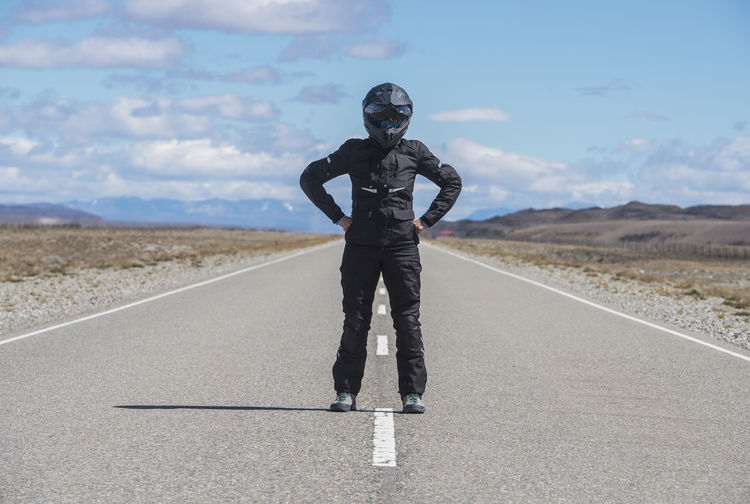 Woman in motorbike gear standing in the middle of empty highway