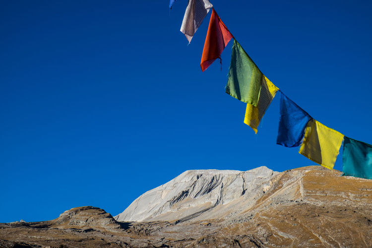 Low angle view of prayer flags hanging against clear blue sky