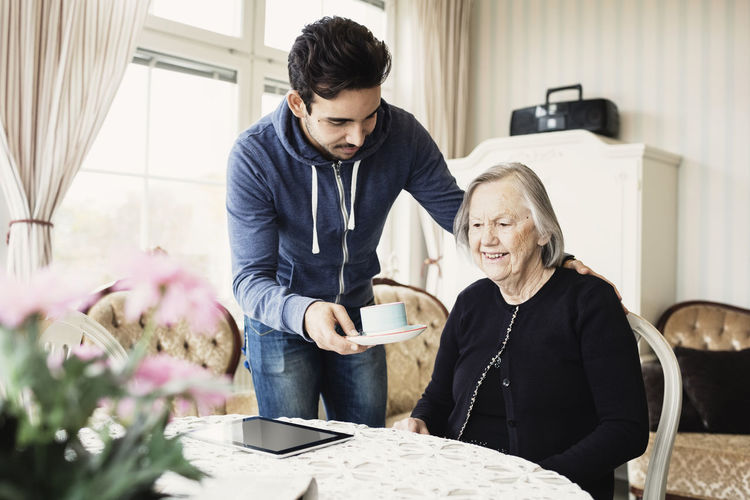 Caretaker serving coffee to senior woman sitting at nursing home