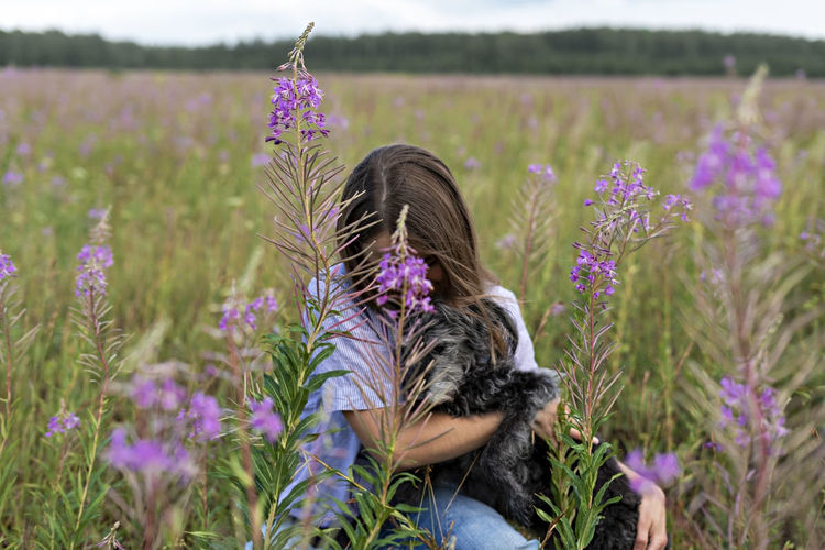 Young woman holding fluffy senior dog in hands in field of fireweed flowers pet love, dog walking 