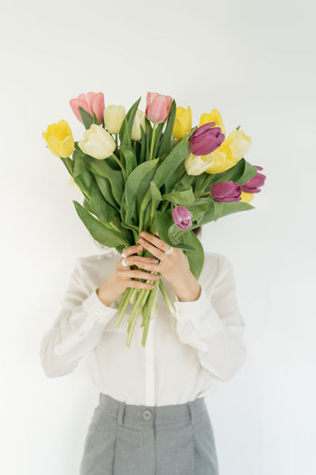 Midsection of woman holding flowers against white background