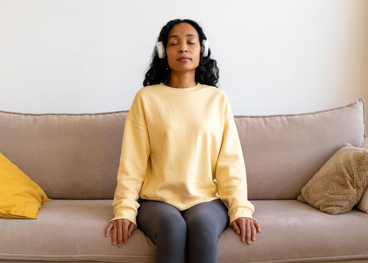African-american female sitting on couch and listening to music in headphones. breathing therapy