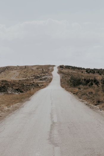 Dirt road amidst land against sky