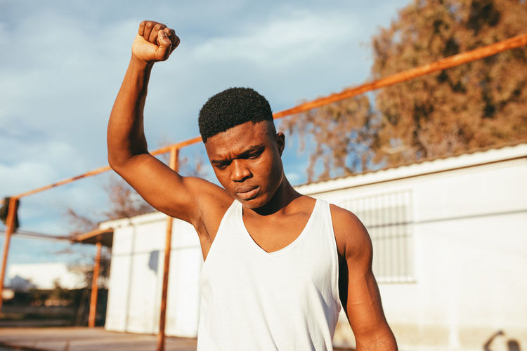 Young man with arms raised standing against sky