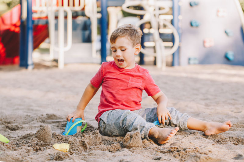 Boy with mouth open playing with toy on sand at playground